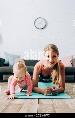 Selective focus of sportswoman doing plank near baby girl on fitness mat Stock Photo