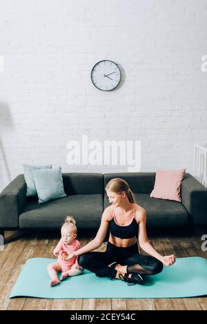 Mother in sportswear sitting in yoga pose near infant daughter on fitness mat Stock Photo