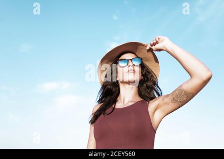 Carefree female traveler in summer dress and sunhat walking along empty roadway and looking away while enjoying freedom Stock Photo