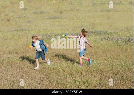 Positive brothers in summer wear running in meadow and playing with water guns while entertaining during weekend in countryside Stock Photo
