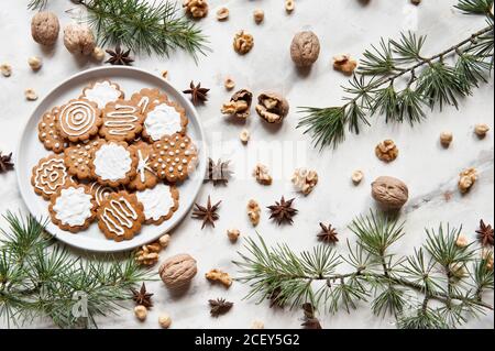 Top view composition with sweet homemade Christmas cookies decorated with white sugar icing served on plate placed on white table near various nuts and fir branch Stock Photo