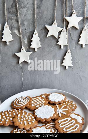 Plate with assorted gingerbread cookies with white icing placed near gray wall decorated with craft star and tree shaped paper items Stock Photo