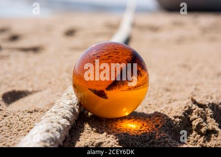 Orange glass ball on sand near the sea. Abstract conceptual photo. Stock Photo