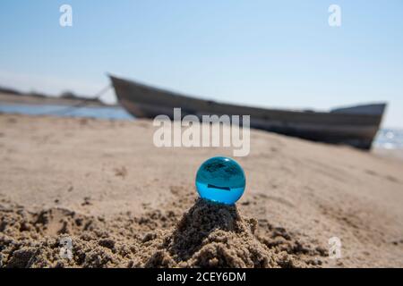 Blue glass ball on sand near the sea. Abstract conceptual photo. Stock Photo