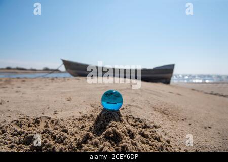 Blue glass ball on sand near the sea. Abstract conceptual photo. Stock Photo