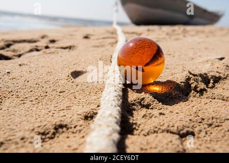 Orange glass ball on sand near the sea. Abstract conceptual photo. Stock Photo