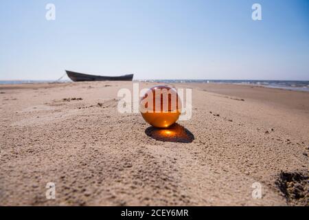Orange glass ball on sand near the sea. Abstract conceptual photo. Stock Photo