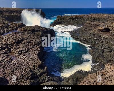 Buracona - The Blue Eye of Cabo Verde - blue lagoon inside a black rock with ocean splash in the back Stock Photo