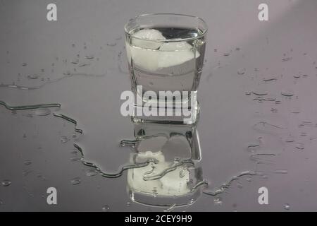 Bartender pouring up frozen vodka from a bottle into two shots glasses with ice cubes against black background. Stock Photo