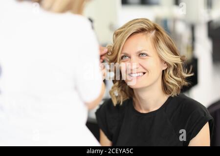 Master hairdresser straightens the hair of client's woman. Stock Photo