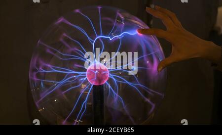 Interactive exposition in science museum. Woman touching plasma ball. Electricity and physics concept Stock Photo