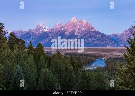 Pink light of dawn shines on the Teton mountains and the Snake river as seen from the Snake River overlook in Grand Teton National Park Stock Photo