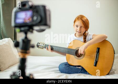 cute adorable child blogger play guitar, talk at camera how she learned playing acoustic guitar, she is self-taught Stock Photo