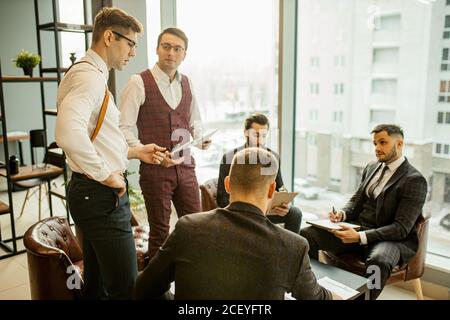 young confident men developing new business startup, discussing interaction in finance and market, sharing opinions and ideas with each other, dressed Stock Photo
