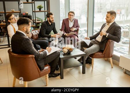successful interaction of young leaders in tux gathered together for discussing business ideas and projects, developing new business startup, solving Stock Photo