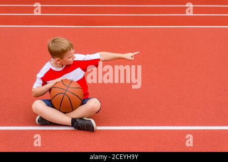 Boy posing with basketball ball on artificial red turf. Sports training in the field. Kid sport online concept Stock Photo