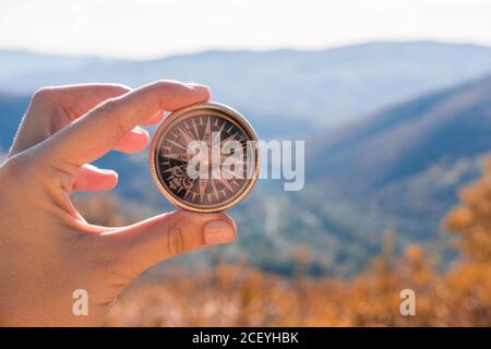 Female hand of traveler, hiker with compass on background autumn forest landscape with mountains on the horizon in orange colors in fall Stock Photo