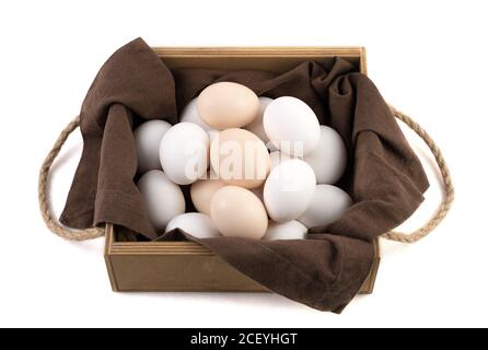 Chicken eggs are white and brown in a beautiful wooden package with a brown linen napkin. Stock Photo