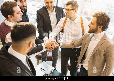 young caucasian business co-workers joined hands in one,dressed in formal suits, successful cooperation of business people. success depends on cohesio Stock Photo