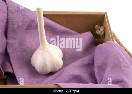 White garlic isolated on a white background, side view, placed in a wooden box with a purple napkin. Stock Photo