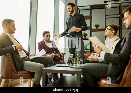 young confident men developing new business startup, discussing interaction in finance and market, sharing opinions and ideas with each other, dressed Stock Photo