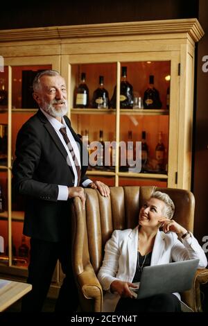 Satisfied European man looks to camera with happy expression, stands behind charming caucasian woman, poses against wall with various items Stock Photo