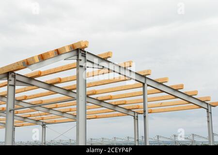 Wooden roof beams on the steel frame of a building under construction. Construction of an agricultural hangar. Building frame Stock Photo