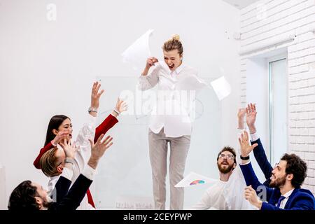 beautiful slim woman leader stand on table, shine from happiness, celebrating good job of co-workers in modern office. happy business team concept Stock Photo