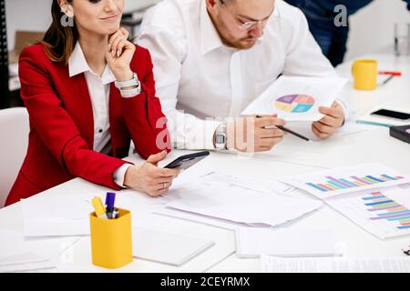 cropped young woman and man having coversation, discussing new business project together, successful team of two people holding documents, papers with Stock Photo