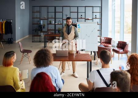 Young arabian business coach giving presentation to executive managers team explaining strategy in modern office, senior company leader presenting emp Stock Photo