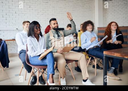 overjoyed diverse workers or company interns listening to presenter or coach at meeting and ask questions Stock Photo