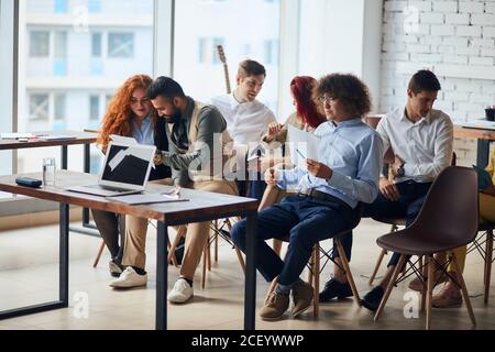 multiethnic group of young workers discuss ideas engaged in educational meeting with business coach, employees involved in teambuilding activity Stock Photo