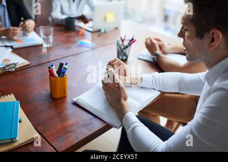 While working in office. Young business leaders sitting on table in the process of co-working, writing Stock Photo