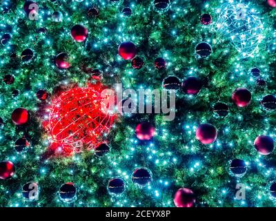 The branches of a Christmas tree with many different balls and garlands are illuminated in the dark. Background texture Stock Photo