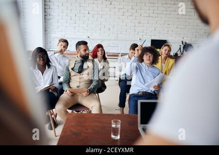 multiethnic group of young workers discuss ideas engaged in educational meeting with business coach, employees involved in teambuilding activity Stock Photo