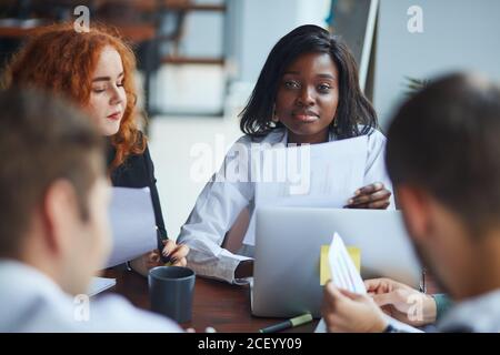 multi-ethnic team of co-workers having a brainstorming session sitting around a table together with laptops in the office as they plan their business Stock Photo