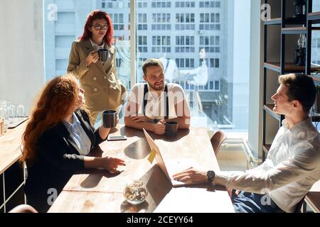 Lively discussion between young businessmen, female investor and personal assistant and having coffee during a business appointment. Professionals sha Stock Photo