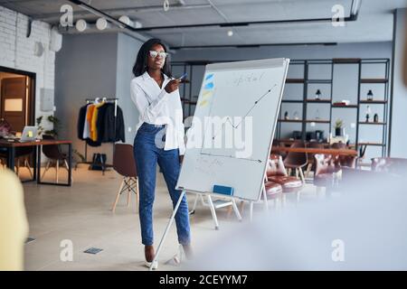 black businesswoman stand talking explaining making flip chart presentation for office employees using diagrams, motivated african American speaker co Stock Photo