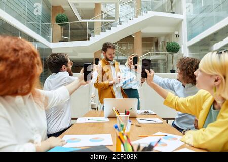 Attractive team leader demonstrates samples of colour for design project, engaged people raise hands with cell phones to take a photo, designers agenc Stock Photo