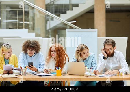 young cheerful interior designers, sit at working table, do daily routine job, solve business problems, discuss new design project, express optimistic Stock Photo