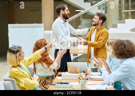 Handsome smart guy with stylish beard, smiles broadly, shakes hand with satisfied tall partner, takes congratulations, expressess happiness, designers Stock Photo