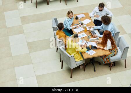 Playful delighted designers sit at table, peacefully discuss work related issues in modern office, satisfied with result of communication, high angle Stock Photo