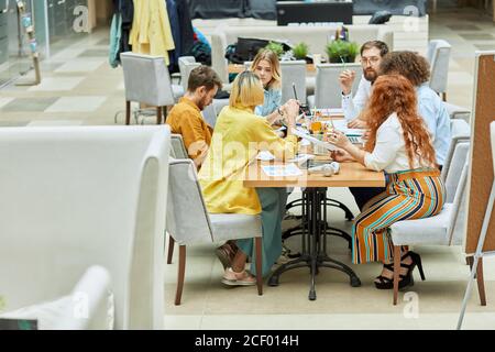 Group of concentrated busy graphic designers thinking over new project, siting at table full of paper and stationary items, brainstorming concept Stock Photo