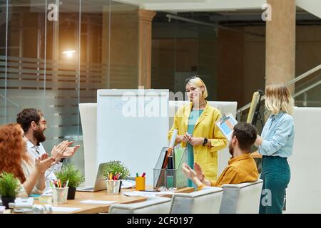 Optimistic impressed designers applauses to young cheerful satisfied colleague after good creative presentation of cool ideas. Concept of young design Stock Photo