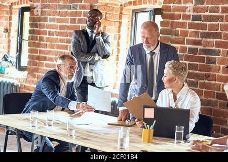 Creative director blond woman wear white office shirt check plan new product, which create caucasian man wear suit. Man near table advice change produ Stock Photo