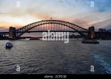 Sydney Harbour Bridge at sunset viewed from on the water of Sydney harbour. Harbour vessels and boats can be passing by the bridge. Australia. Stock Photo