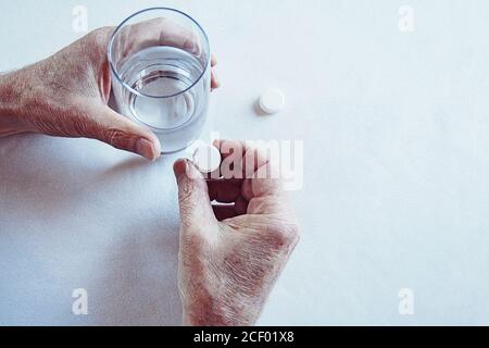 Elderly man hands taking medicine pill with a glass of water Stock Photo