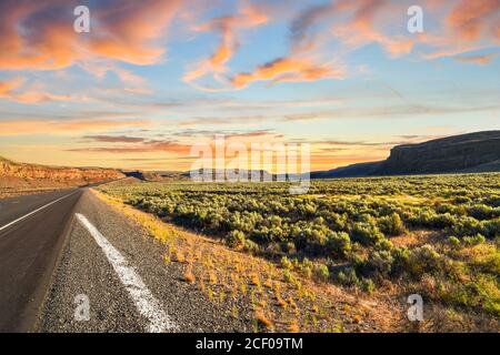 Long road winding though the flat desert brush land into the mountains of the Inland Northwest of rural Washington State in the American Desert Stock Photo