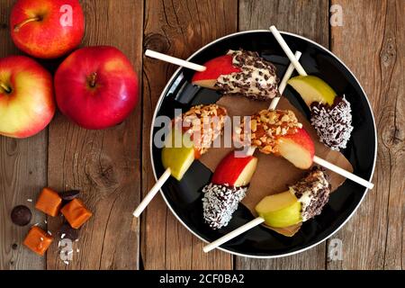 Plate of mixed sweet caramel and chocolate dipped apple slices, overhead scene on rustic wood Stock Photo