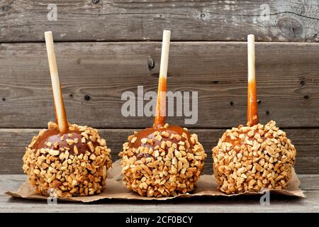 Three festive caramel apples with nuts against a rustic wood background Stock Photo